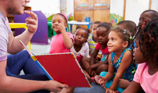 Group of children looking at teacher holding a picture book